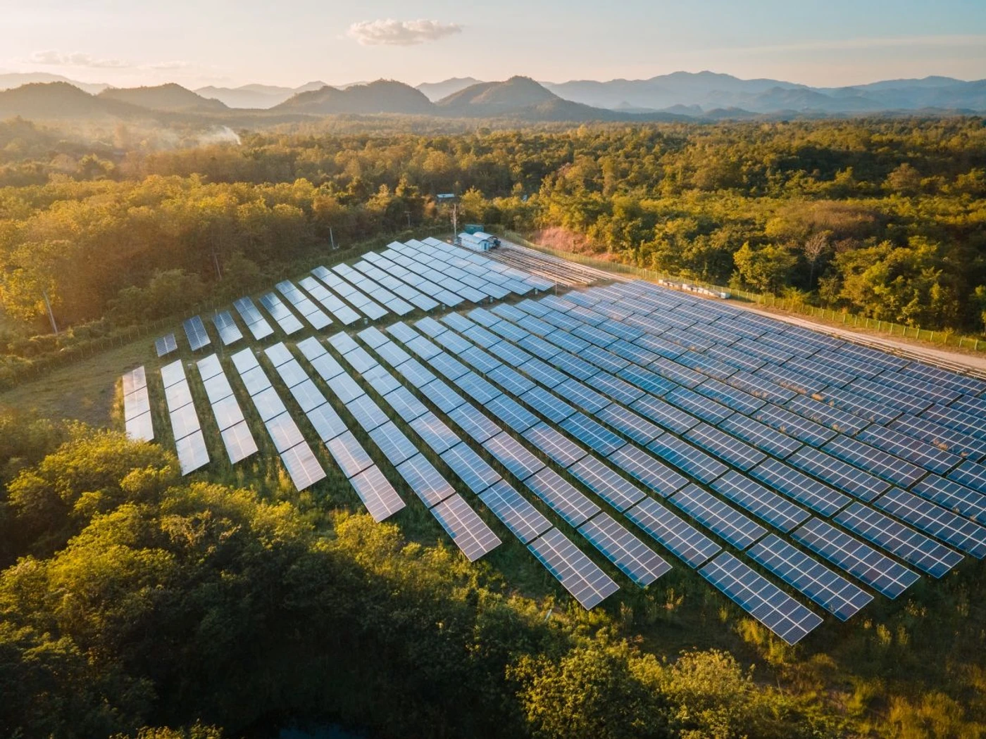Photovoltaik-Freiflächenanlage in hügeliger Landschaft bei Sonnenuntergang.